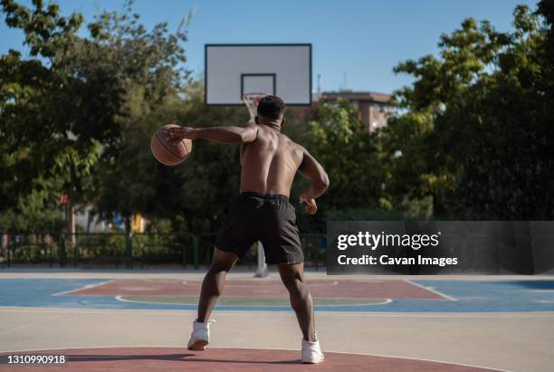 unrecognizable black man dribbling ball near hoop - streetball stock pictures, royalty-free photos & images