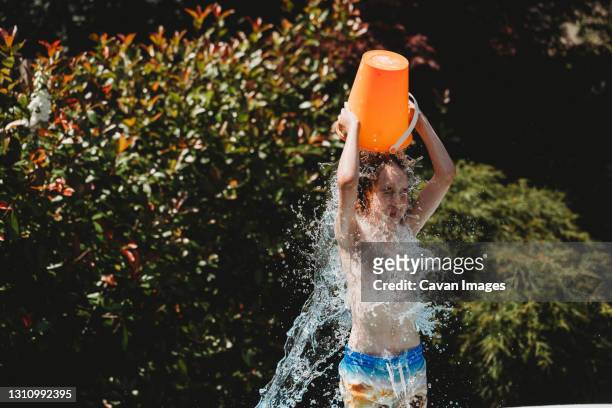 boy standing pouring bucket of water over his own head - hot weather stock pictures, royalty-free photos & images