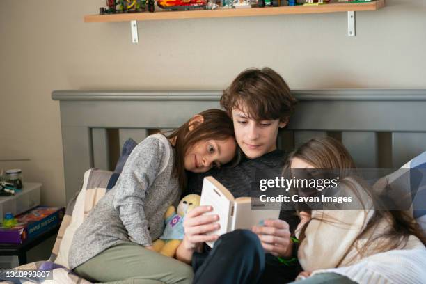 tween boy reading to his little sisters in bedroom. - sister stockfoto's en -beelden