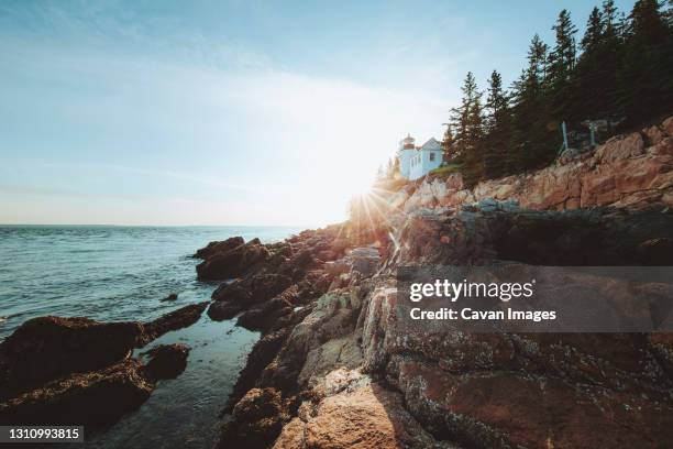 the sun sets behind bass harbor head lighthouse along a rocky coast. - bedrock fotografías e imágenes de stock