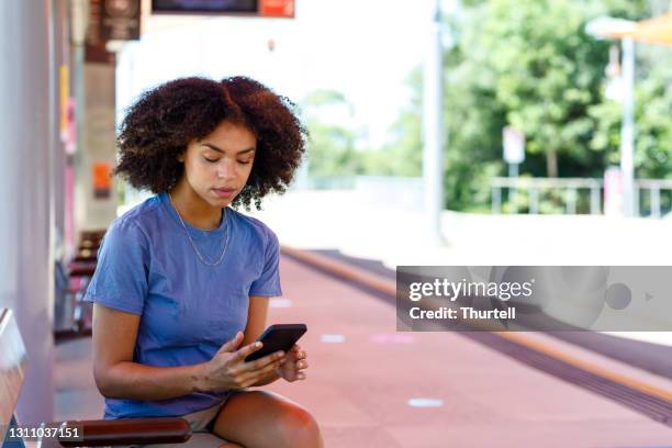 mulher afro-australiana usando telefone esperando trem chegar - nativo da áfrica - fotografias e filmes do acervo