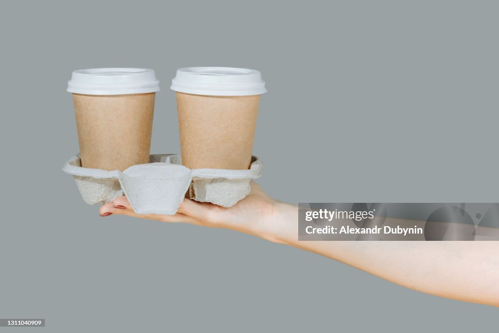 Two brown disposable coffee cups on a cardboard rack isolated on a gray background. Hygienic cooking or home delivery concept. Banner, template, copy space
