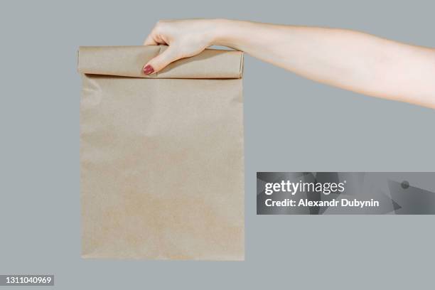 smiling young girl in white clothes isolated on gray background. delivery service from store or restaurant concept. hold brown takeaway kraft paper with food credit card. woman copy space - hands full stock pictures, royalty-free photos & images