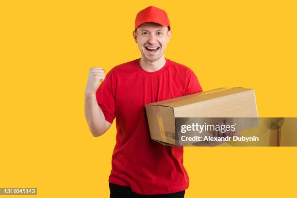 home delivery service. courier delivery man to a red uniform holds a corton box on a yellow isolated background. copy space - giving a box ストックフォトと画像