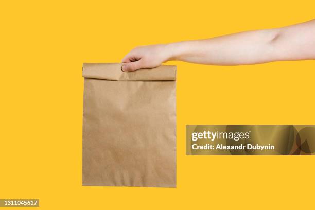 delivery service service concept. male hand holding eco craft takeout food bag on isolated yellow background studio. packaging mock up template. copy space - box packaging mockup stock pictures, royalty-free photos & images