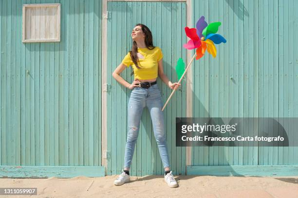 woman with a colorful pinwheel in front of a wooden house - 両手を腰に当てる ストックフォトと画像