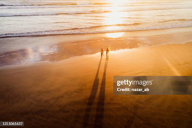 two women carrying surfboard on beach at sunset time. - new zealand beach stock pictures, royalty-free photos & images