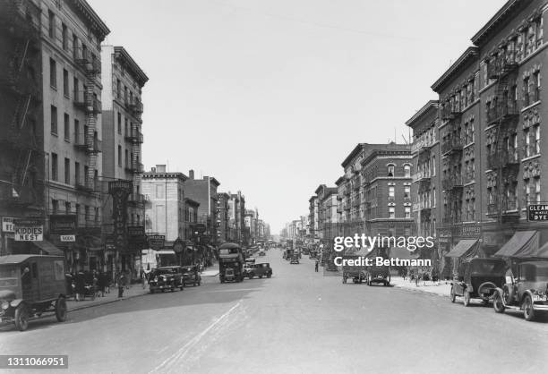 Vehicles parked alongside the sidewalk on St Nicholas Avenue, fire escapes rising above the shops on street level in the Bronx, New York City, New...