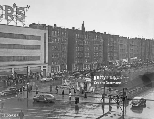People queue on the sidewalk in heavy rain to buy nylon stockings from Alexander's department store at Grand Concourse and Fordham Road in the Bronx,...
