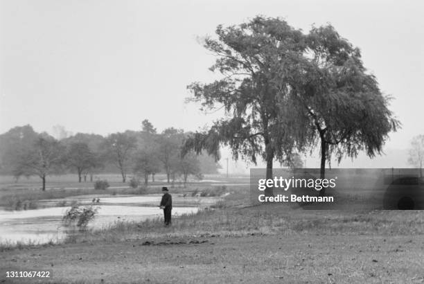 Lone fisherman standing in the rain on the bank of the Flushing River in Flushing Meadows in the Queens borough of New York City, New York, 23rd...
