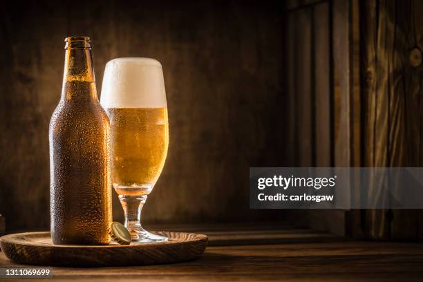 bierflasche mit einem trinkglas voller bier auf einem rustikalen holztisch - bierflasche stock-fotos und bilder