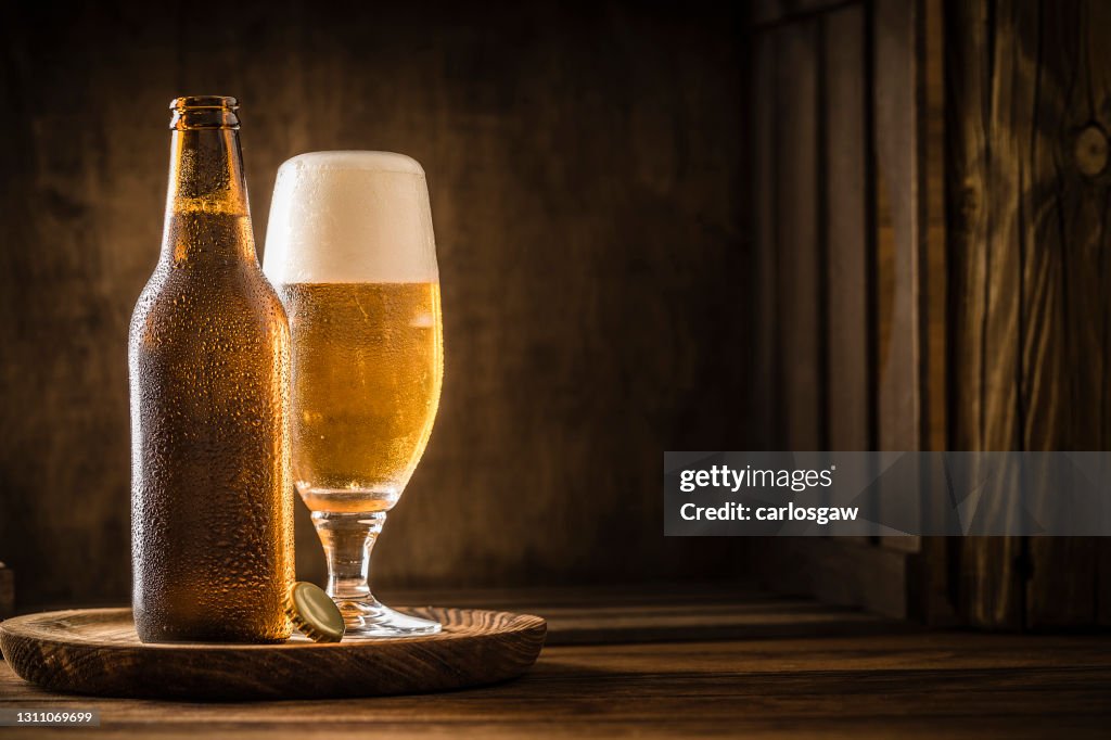 Botella de cerveza con un vaso lleno de cerveza en una mesa de madera rústica