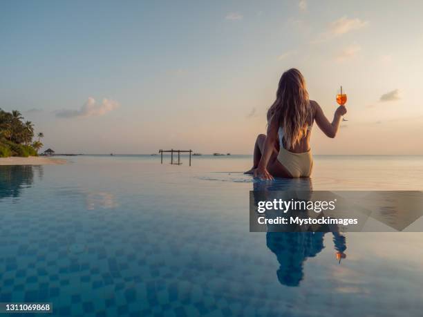 woman drinking cocktail at sunset in an infinity pool - tropical drink stock pictures, royalty-free photos & images