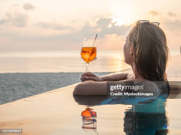 女人在日落時分在無邊泳池裡喝雞尾酒 - standing water 個照片及圖片檔