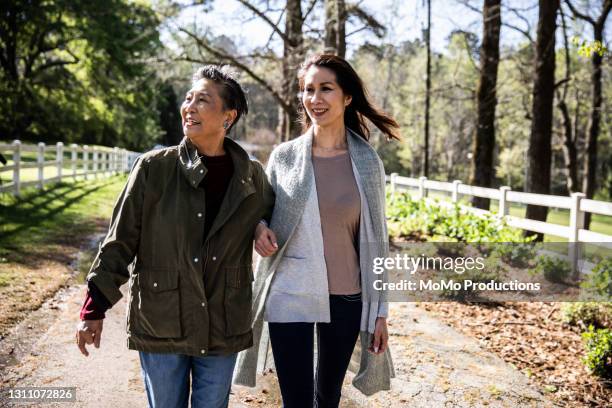 senior mother and adult daughter walking down long farm driveway - asian granny pics stock-fotos und bilder