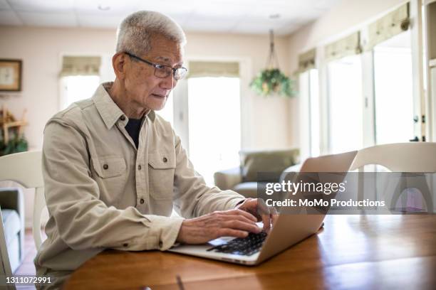 senior man using laptop computer at home - asian old man stock pictures, royalty-free photos & images