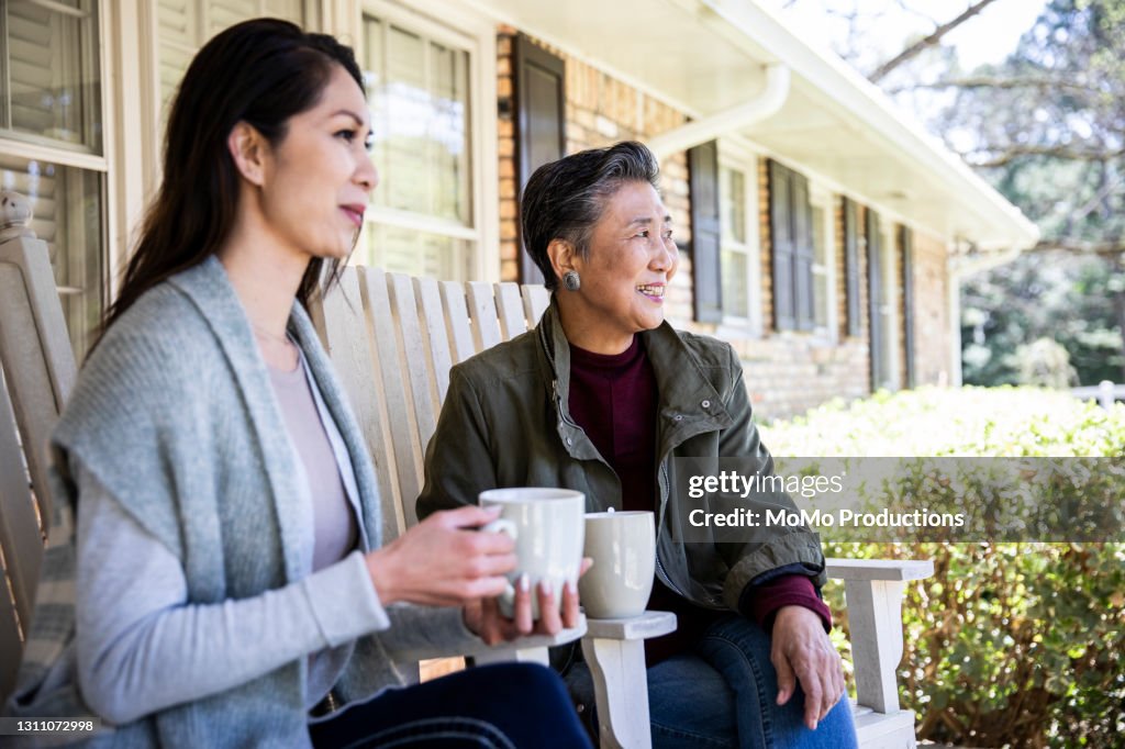 Senior mother and adult daughter having coffee on front porch
