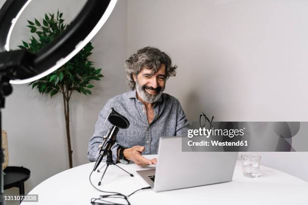 senior male freelancer podcasting with laptop on table at home office - pensioners demonstrate in spain stock pictures, royalty-free photos & images