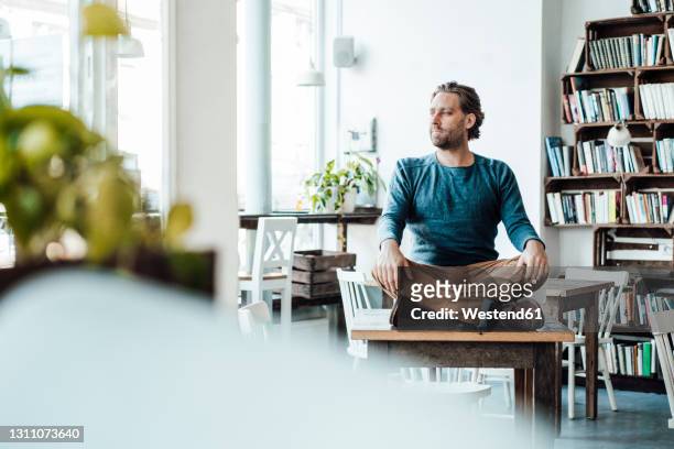 man sitting cross-legged on table in cafe - schneidersitz stock-fotos und bilder