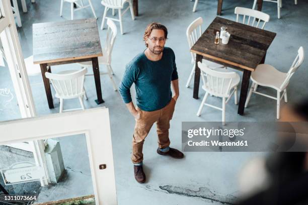 confident male owner with hands in pockets standing at cafe - casual male standing stock-fotos und bilder