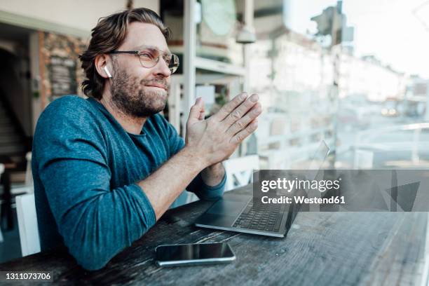smiling manwith hands clasped by laptop in cafe - in ear headphones stock pictures, royalty-free photos & images