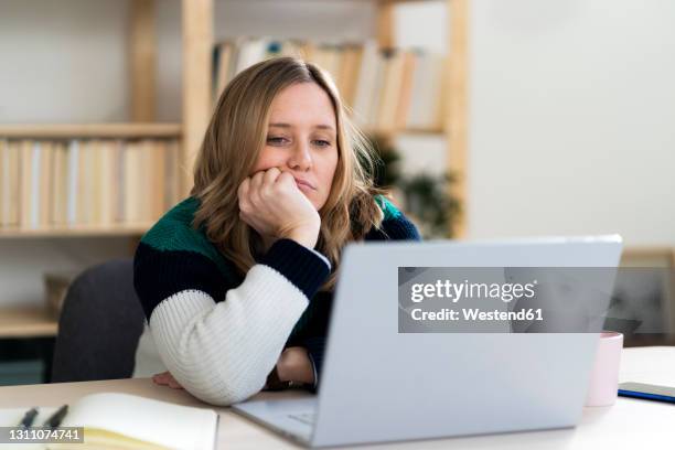 woman with hand on chin staring at laptop - aburrimiento fotografías e imágenes de stock