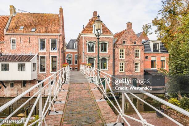 netherlands, groningen province, appingedam, footbridge over damsterdiep canal with brick townhouses in background - groningen city stock-fotos und bilder