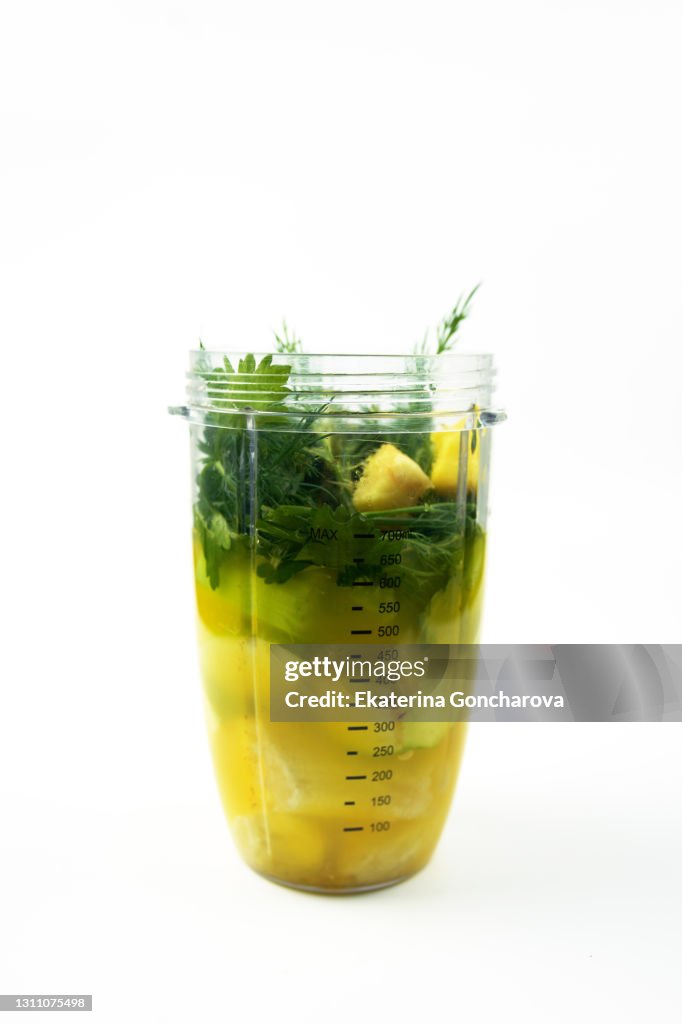 Green fruit and vegetable smoothie in a glass cup before whipping on a white isolated background