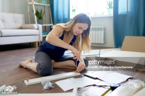 a young woman with the help of instructions makes the assembly of a new table with drawers in her apartment - furniture stock-fotos und bilder
