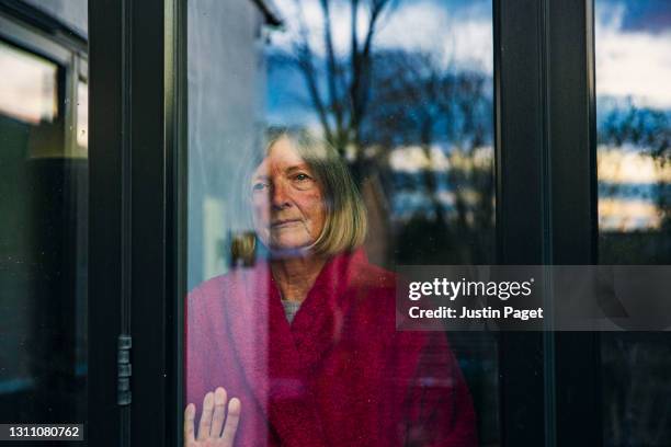 senior woman looking through the window - sliding door stock-fotos und bilder