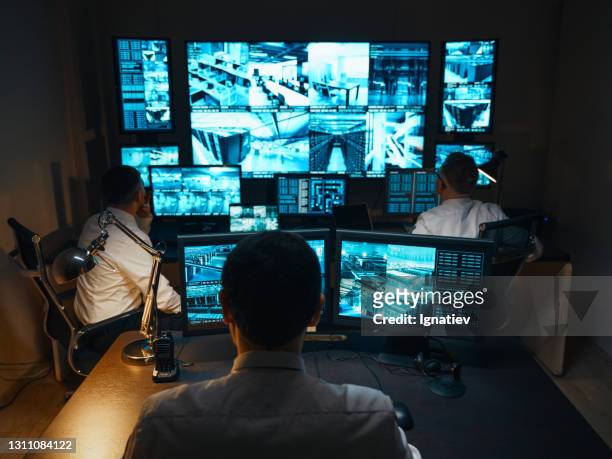 drie bewakers zijn in de beveiligingskamer. ze zitten op werkplekken met grote monitoren die real-time videobeelden van beveiligingscamera's weergeven. de bewakers zijn klaar voor elke mogelijkheid. - beveiligingssysteem stockfoto's en -beelden