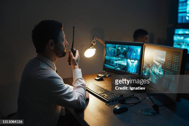 a male security guard at night with a walkie-talkie at the security console closely monitors the security of the object. - equipamento de segurança imagens e fotografias de stock