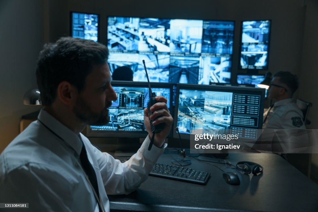 One guard types out a report while another uses a walkie-talkie to talk to the officers on the floor below