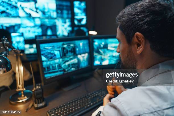 controlador de segurança com conversa de fone de ouvido em uma chamada no escritório de segurança. a sala de escritório está cheia de monitores de computador de mesa com telas de navegação, dados para a equipe. - sala de controle - fotografias e filmes do acervo