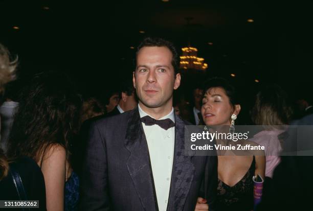 American actor Bruce Willis, wearing a tuxedo and bow tie, with Sherri Rivera in the background, attends the 44th Annual Golden Globe Awards, held at...