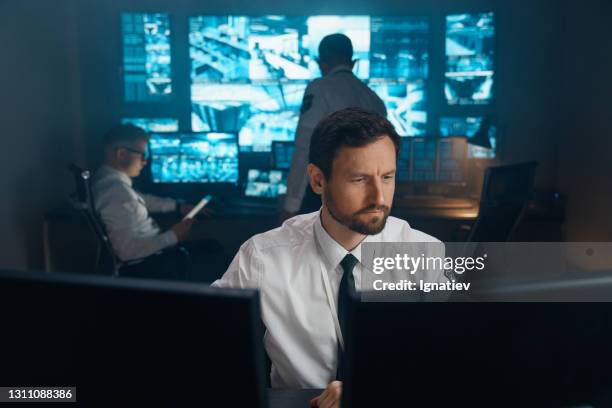 an employee of security, security, police, rescue service, fbi, cia, sits at his workplace behind monitors. - sala de controlo imagens e fotografias de stock