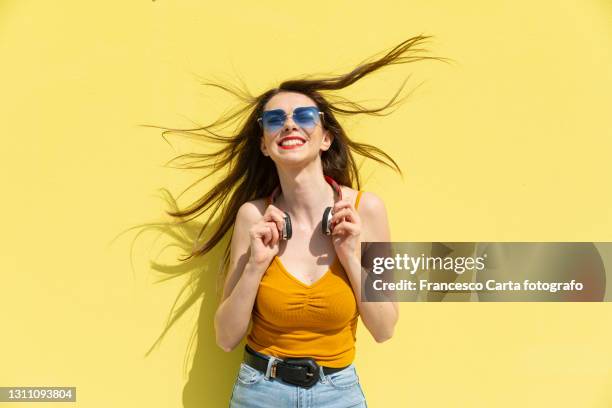 happy young woman with sunglasses and headphones shaking head - person standing infront of wall stockfoto's en -beelden