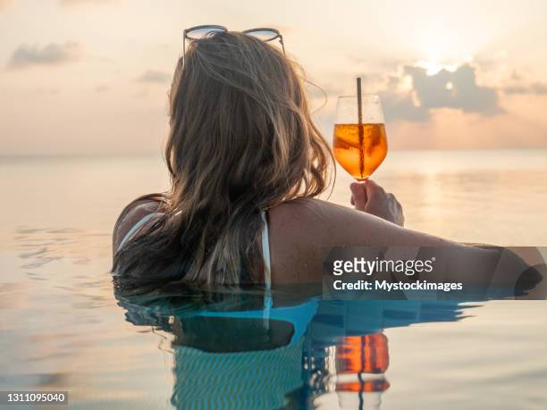 frau trinkt cocktail bei sonnenuntergang in einem infinity-pool - drinkwater kante stock-fotos und bilder