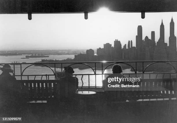 Hotel guests silhouetted as they take in the view of the Manhattan skyline from the roof terrace of the Hotel St George in Brooklyn, New York City,...