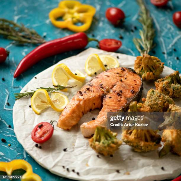 spicy hot red fish baked steak with vegetables, close up shot. sea or river salmon or trout cooked with broccoli, lemon and tomatoes. healthy food concept. soft focus - trout stock photos et images de collection