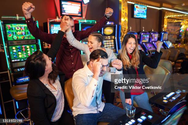 glückliche gruppe von freunden gewinnen, während auf spielautomaten spielen - casino win stock-fotos und bilder