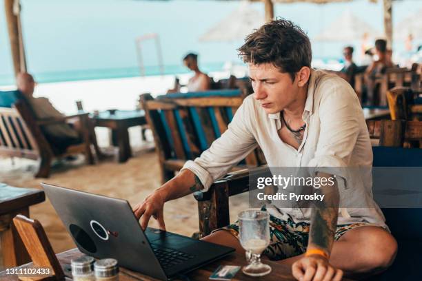 a freelance man works online in a cafe on the beach - itinerant stock pictures, royalty-free photos & images