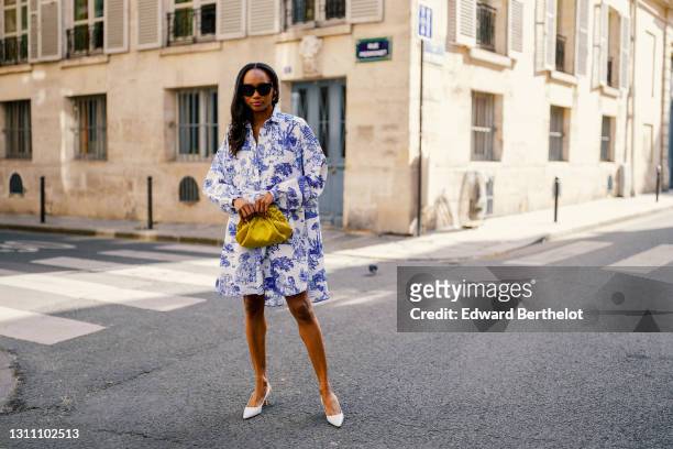 Emilie Joseph @in_fashionwetrust wears sunglasses, a blue and white Toile de Jouy shirt short dress from Moschino, a yellow shiny lime satin pouch...