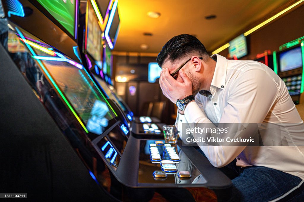 Worried man loosing his money on a slot machine in a casino.