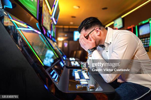 homem preocupado perdendo seu dinheiro em uma máquina caça-níqueis em um cassino. - gambling - fotografias e filmes do acervo