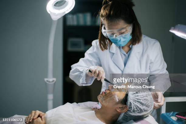 asiatiska kinesiska kvinnor kosmetolog städar sitt kundansikte med bomullsboll innan operationen börjar i operationsrummet - woman applying cotton ball bildbanksfoton och bilder