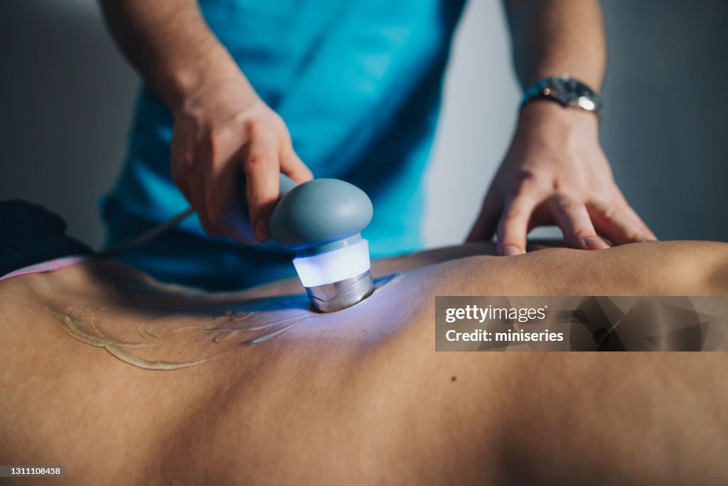 Physiotherapeut mit Ultraschall zur Behandlung des Rückens des Patienten