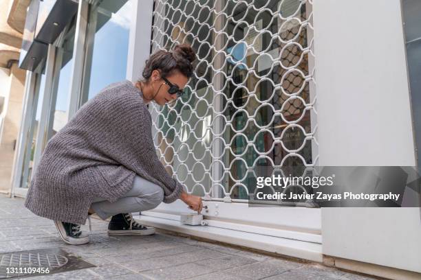 millennial woman openning a small business security grill - cerrar con llave fotografías e imágenes de stock