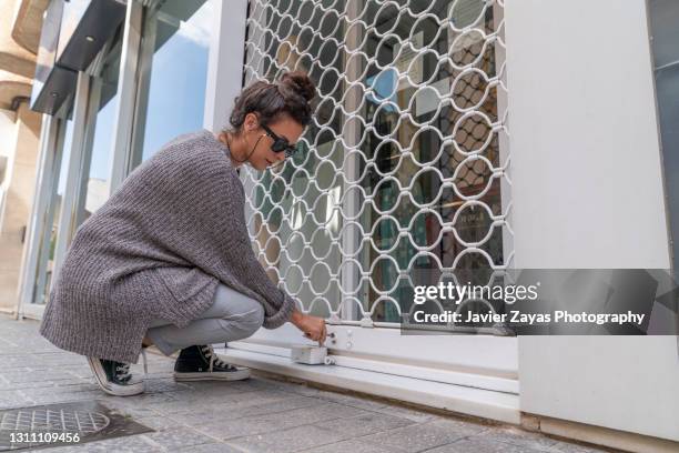 millennial woman openning a small business security grill - closing 個照片及圖片檔