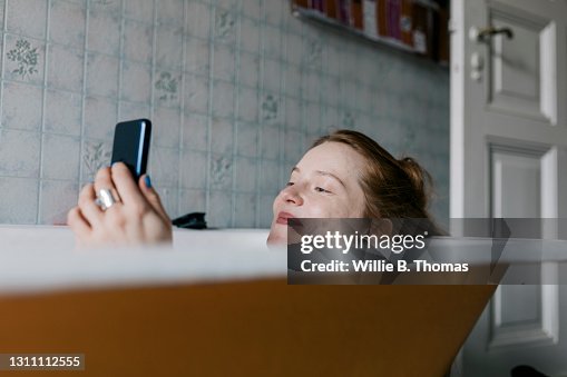 Woman Taking Bath And Smiling While Messaging Someone Woman Taking Bath And Smiling While Messaging Someone